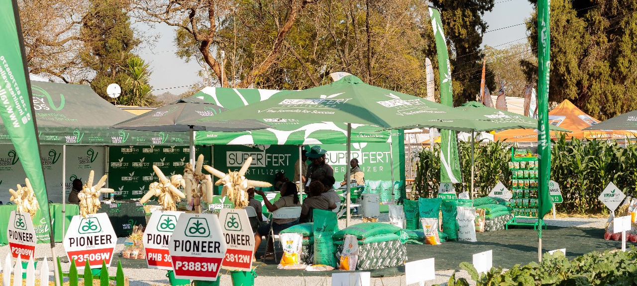 Exhibitors at the Zimbabwe Agricultural Show — green pavilions, branded stands, visitors browsing the showgrounds.